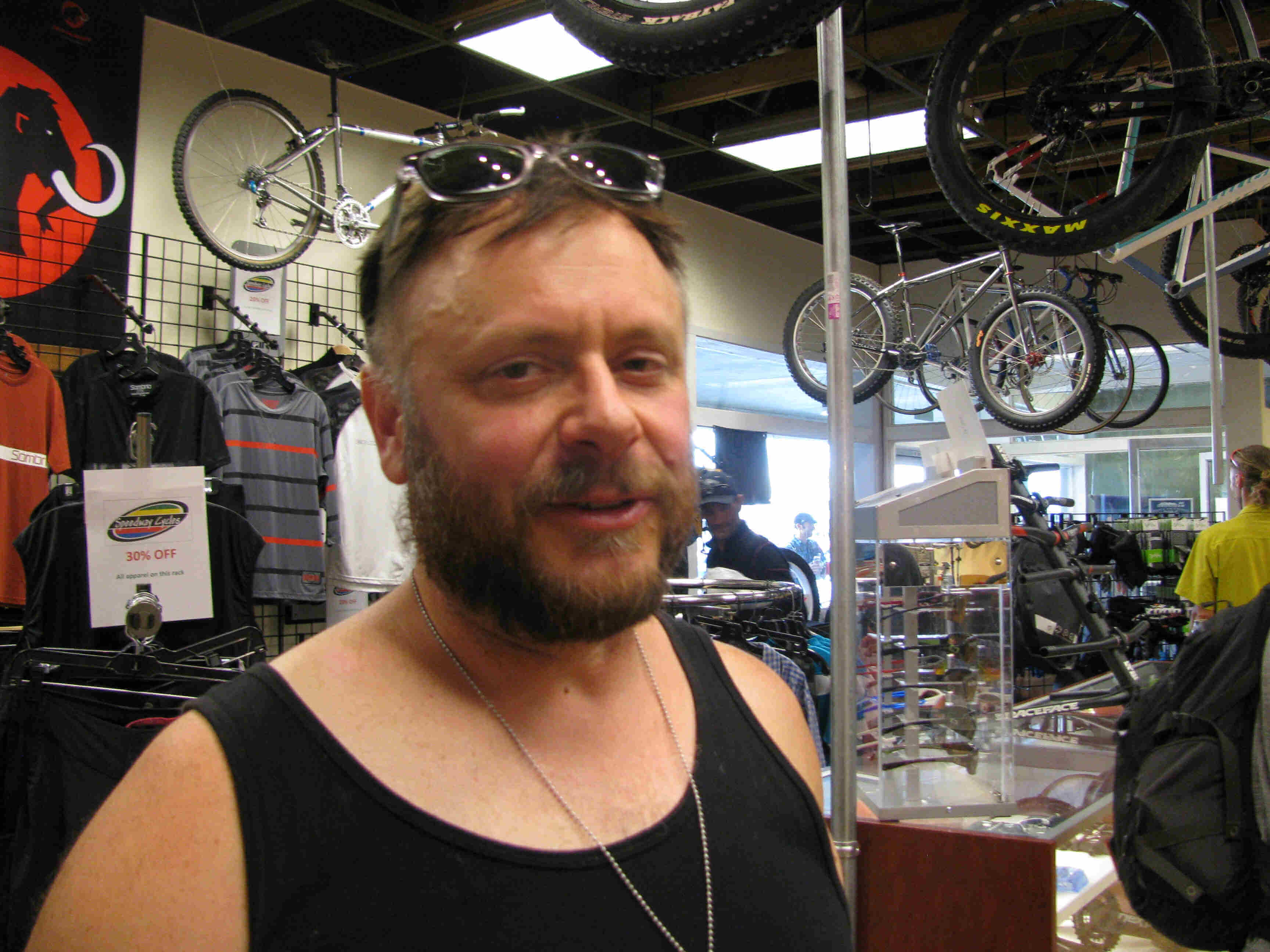 Headshot of a person with a beard and sunglasses on top of their head, standing inside of a bike shop