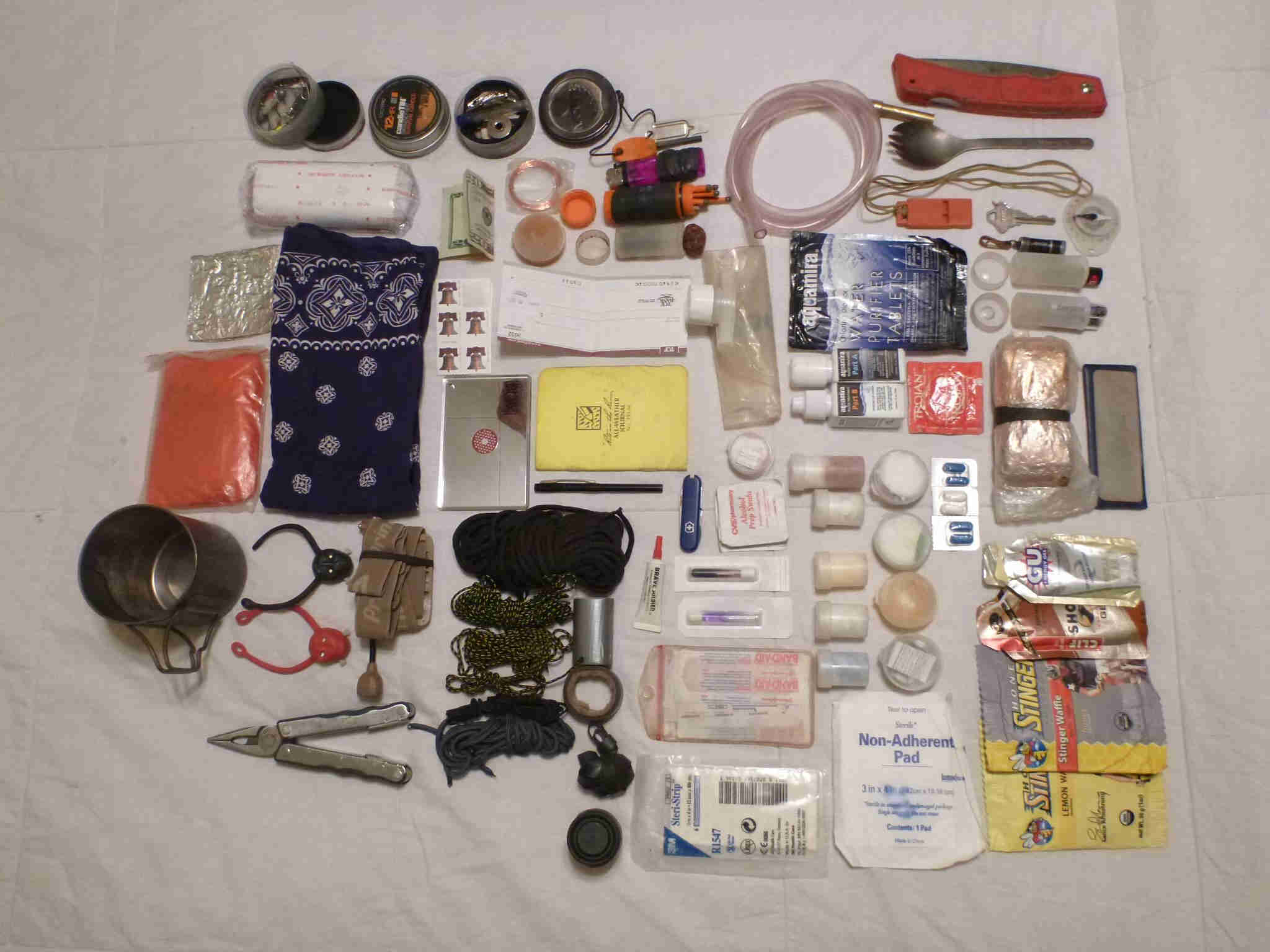 Downward view of all of the components from a person's survival kit, laid out on a flat white surface