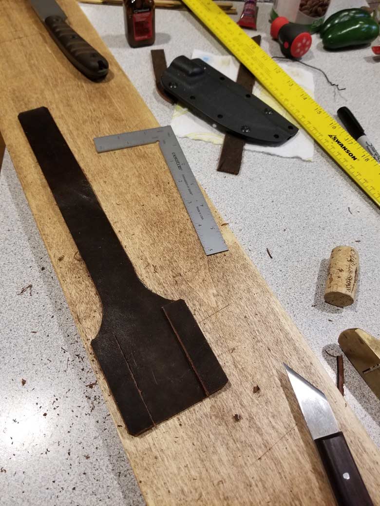 Wooden plank on a workbench with a leather knife, scrap leather and a measure square on top