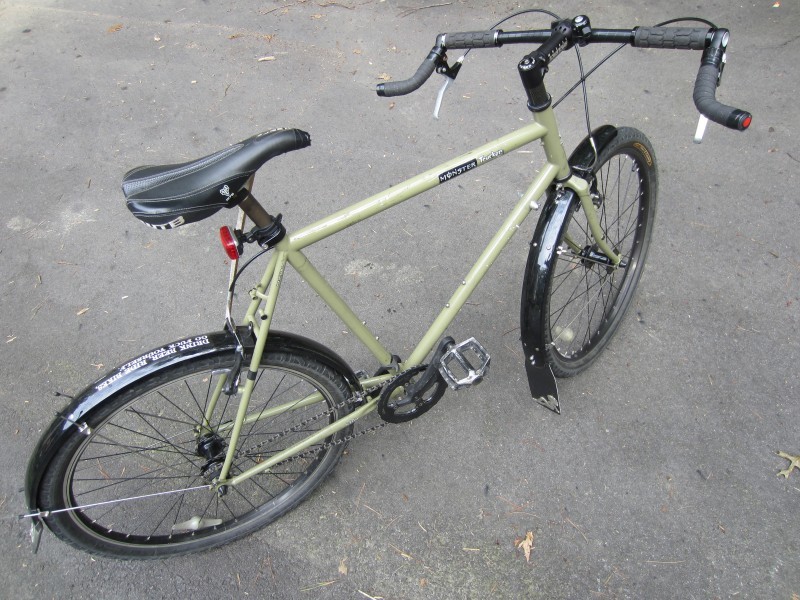 Downward, right side view of a pea green Surly Monster Trucker bike with fenders, parked on pavement