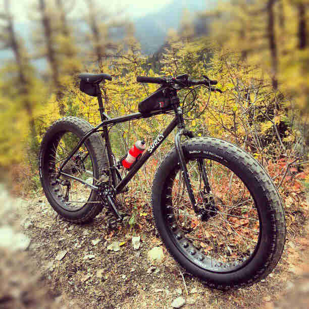 Front right side view of a Surly Moonlander fat bike, black, with a blurred out forest in the background
