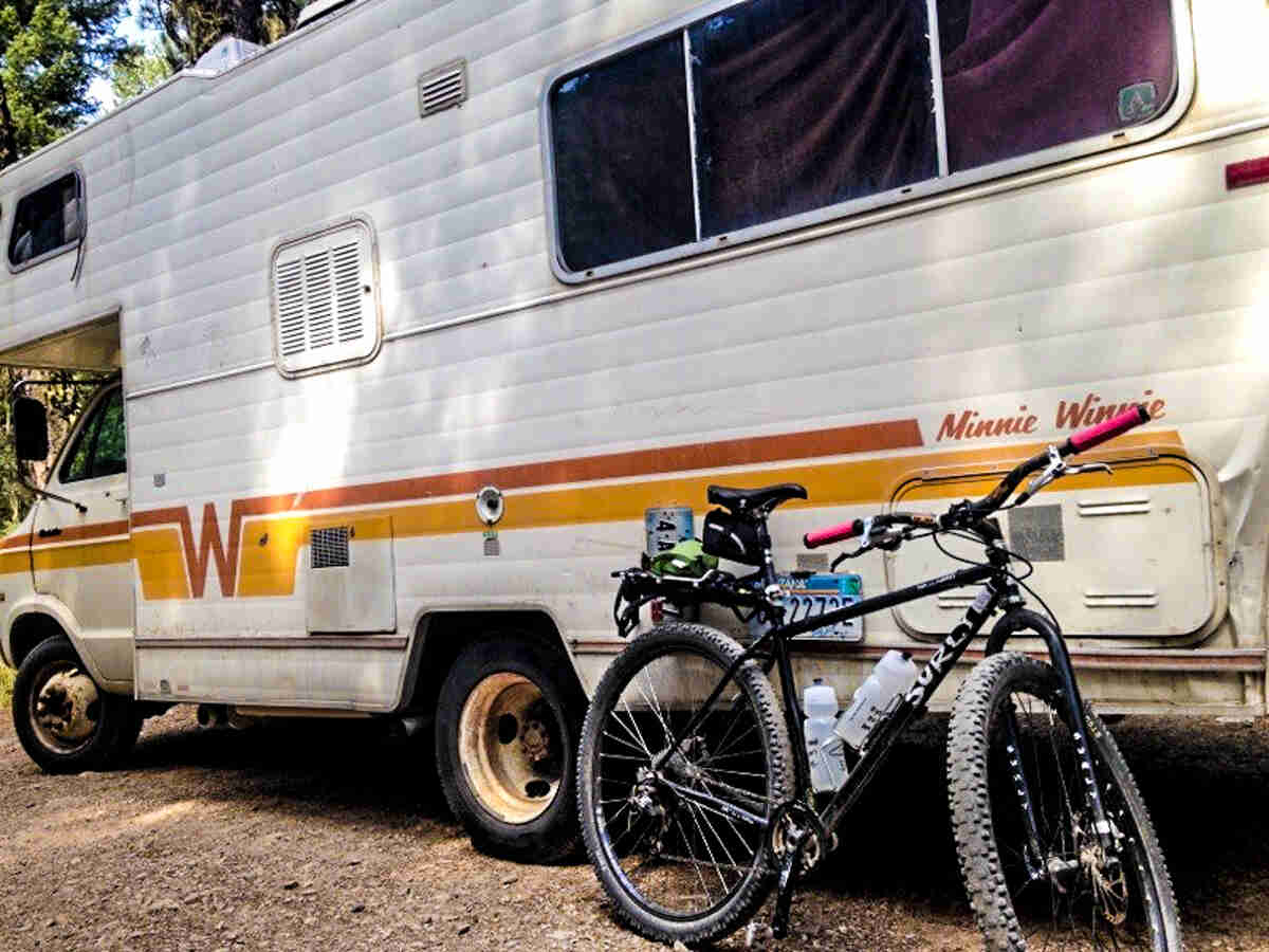 Right side view of a black Surly bike, parked against the rear, left side of a Minnie Winnie RV