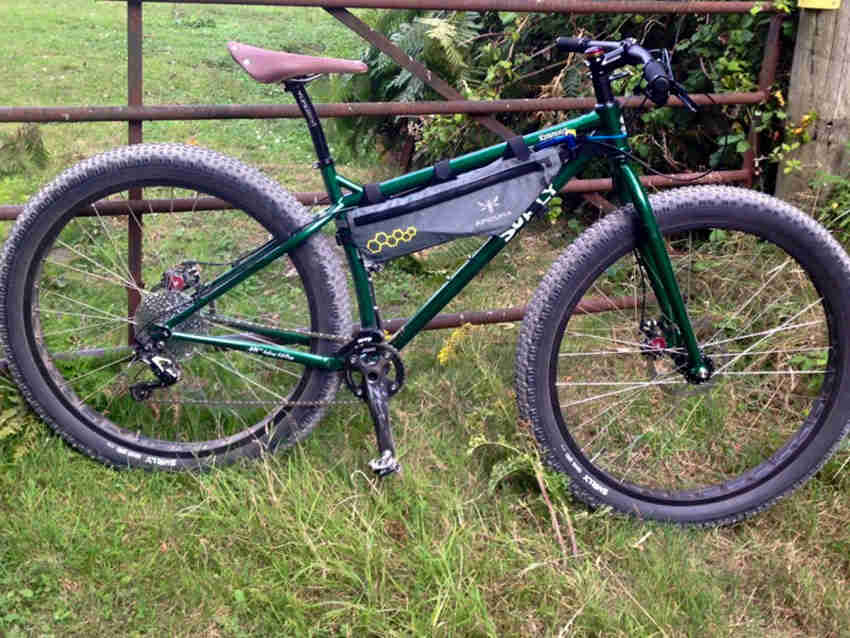 Right side view of a green Surly Krampus bike, with a frame bag, parked on grass in front of a rusty gate