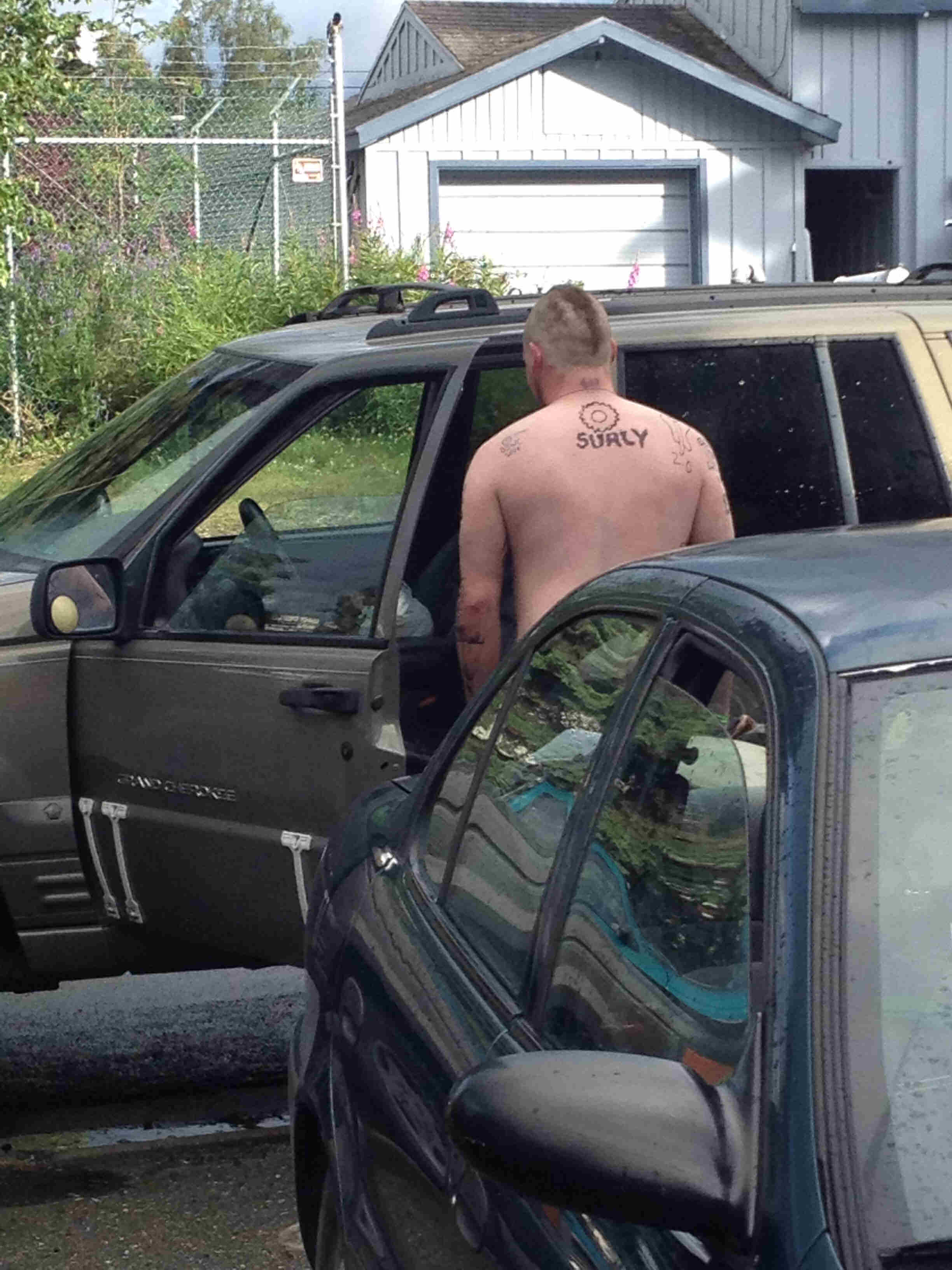 Right view of a person, standing next to an open SUV door,  with a bike gear and, Surly drawn on their back with marker