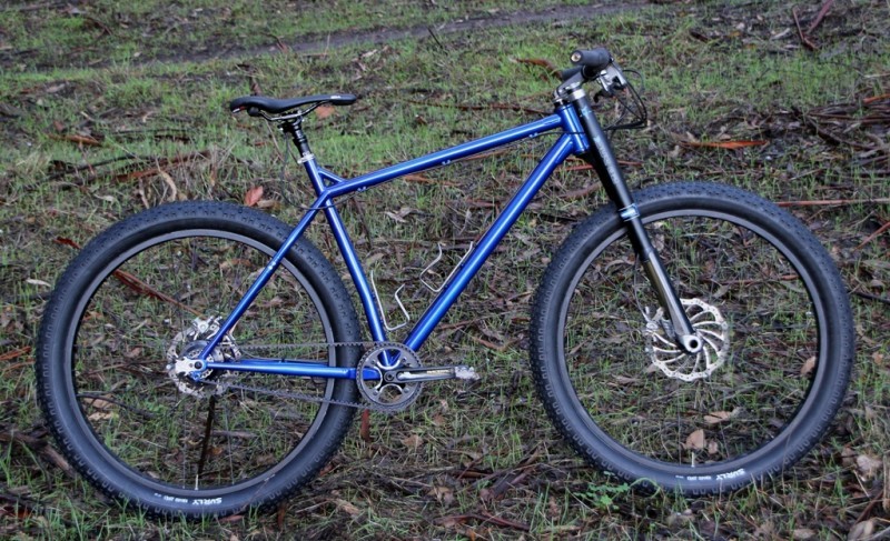 Right side view of a blue Surly Krampus bike, parked in an area with grass and leaves on the ground
