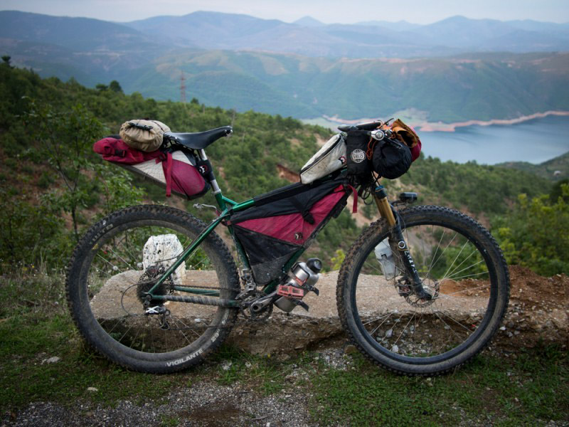 Right side view of a Surly Krampus bike, green, with gear, overlooking  trees, a lake and mountains in the background