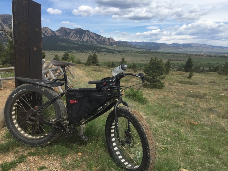 Right side view of a black Surly Moonlander fat bike, parked against a post, with plains and mountains in the background