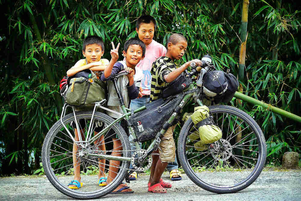 Right side view of a Surly Ogre bike with gear, with 4 children on the left side, and bamboo trees in the background