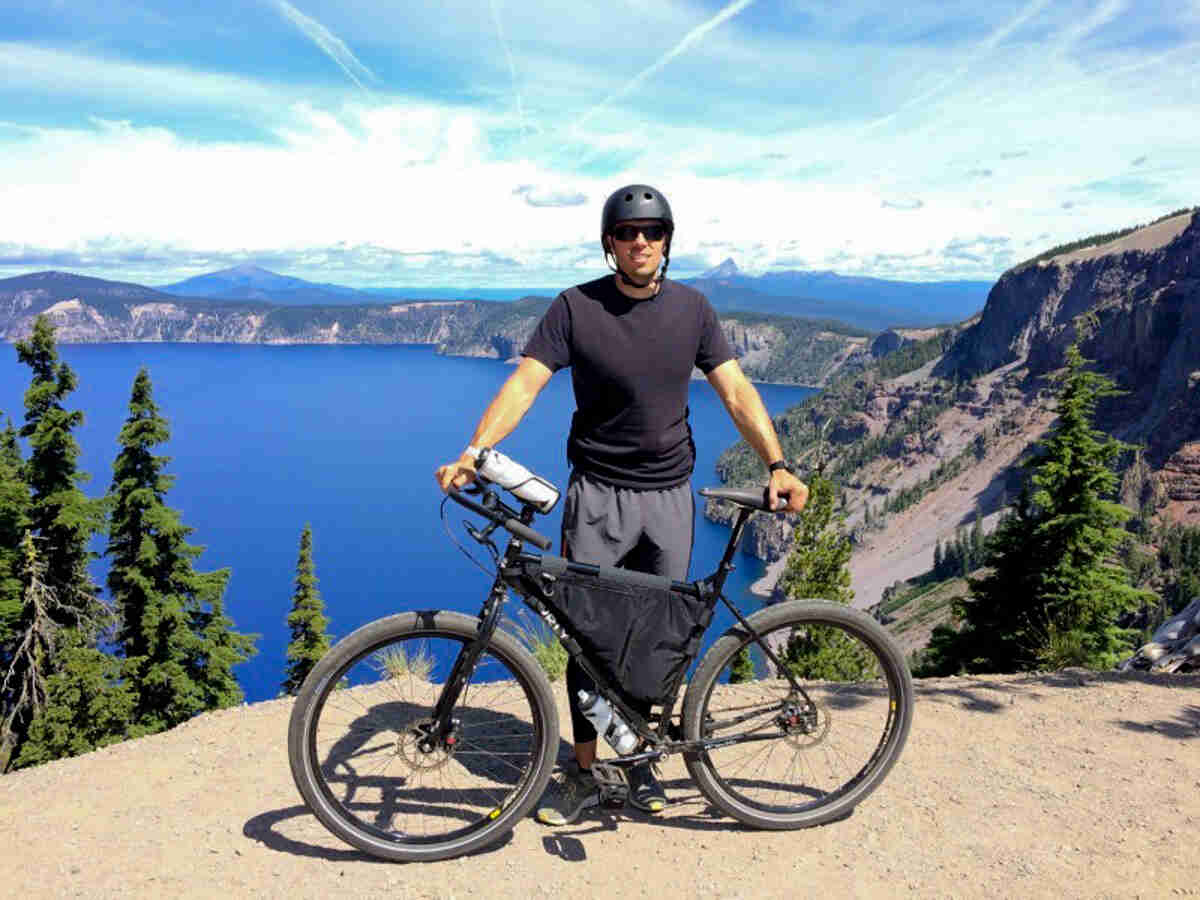 Right side view of a black Surly Ogre bike with a cyclist on the left side, near the edge of a cliff overlooking a lake
