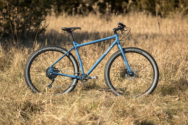 Blue color Surly Ogre complete bike side view propped up in field of tall brown grass on sunny day