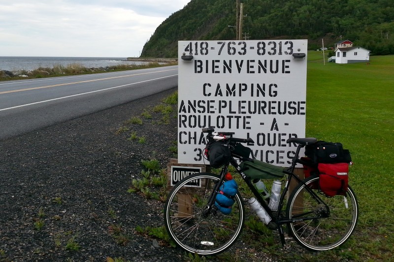 Left side view of a black Surly Ogre bike, leaning on a roadside sign, with green hills and water in the background