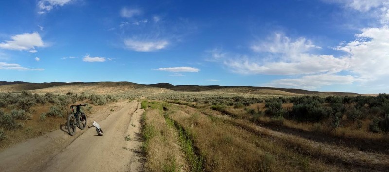 Panoramic, rear view of a Surly Krampus bike, facing down a dirt road running through the plains