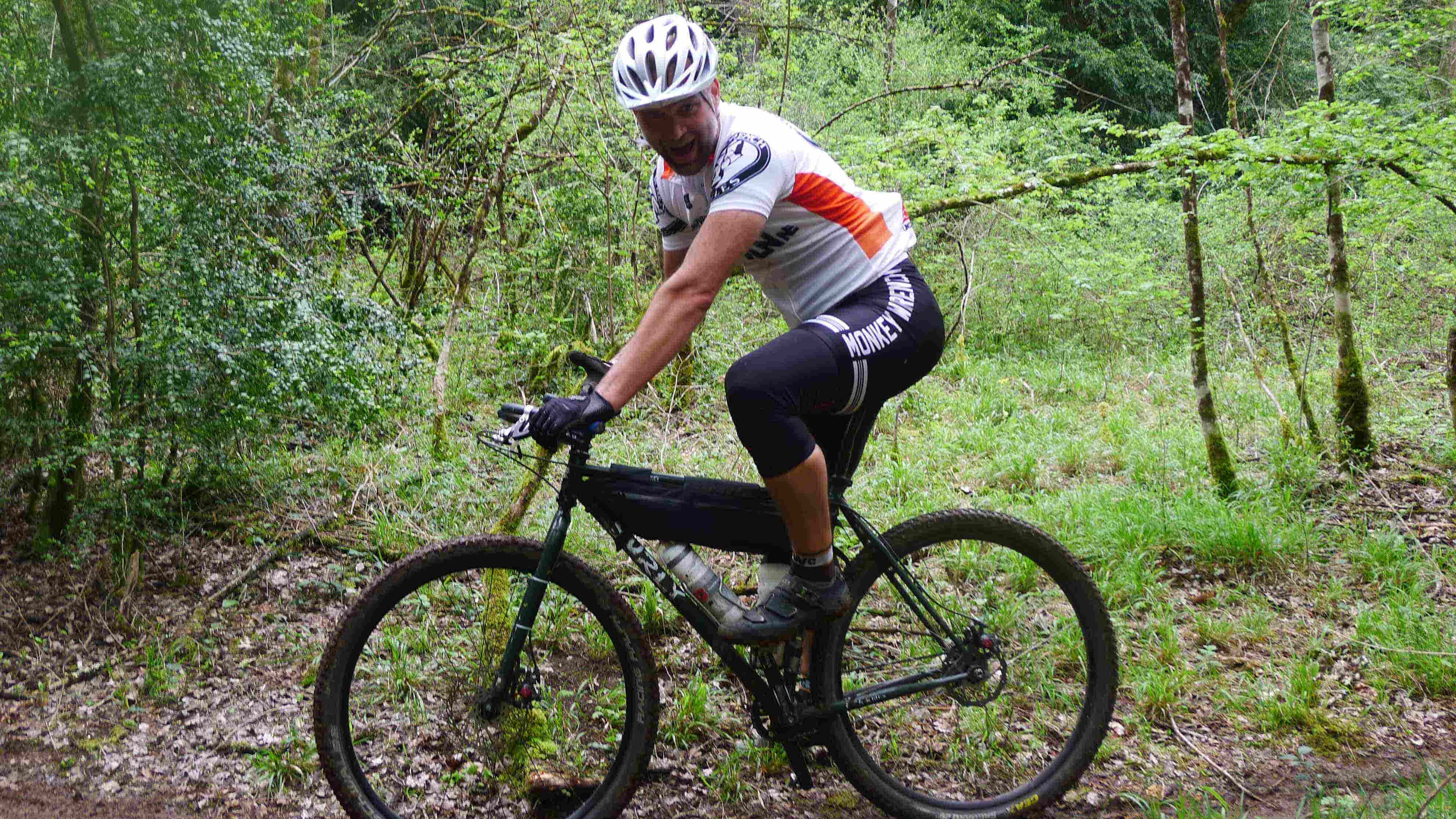 Right side view of a cyclist, riding a black Surly Karate Monkey bike, on a trail in the woods