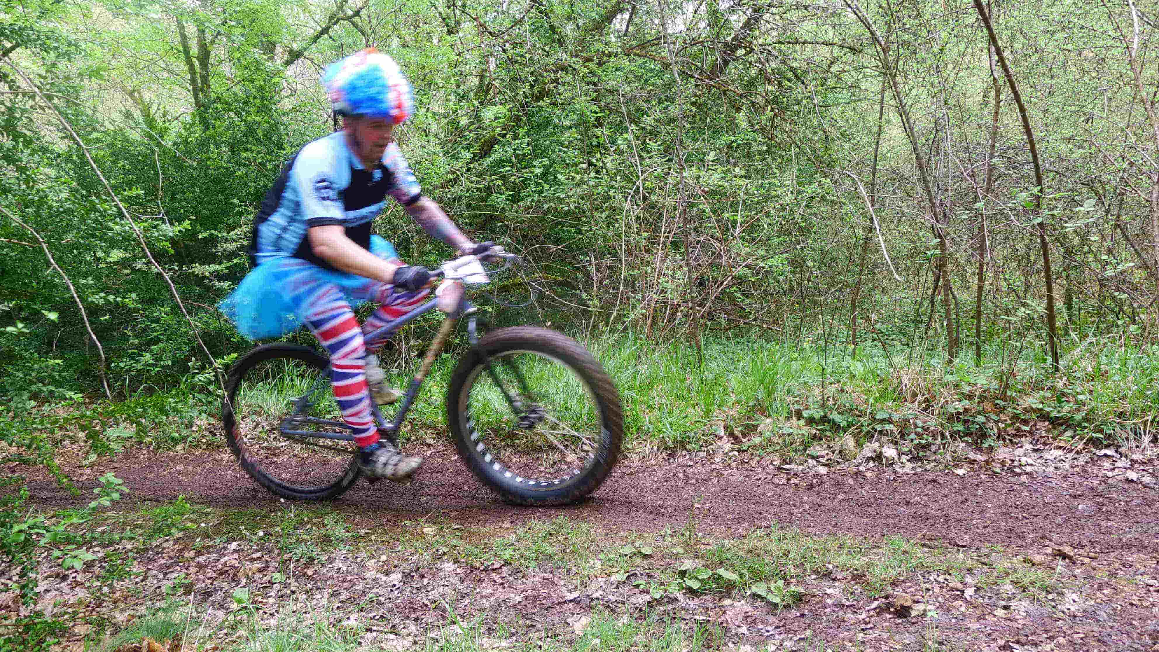 Right side view of a cyclist, wearing a colorful costume, riding a fat bike on a dirt trail in the woods