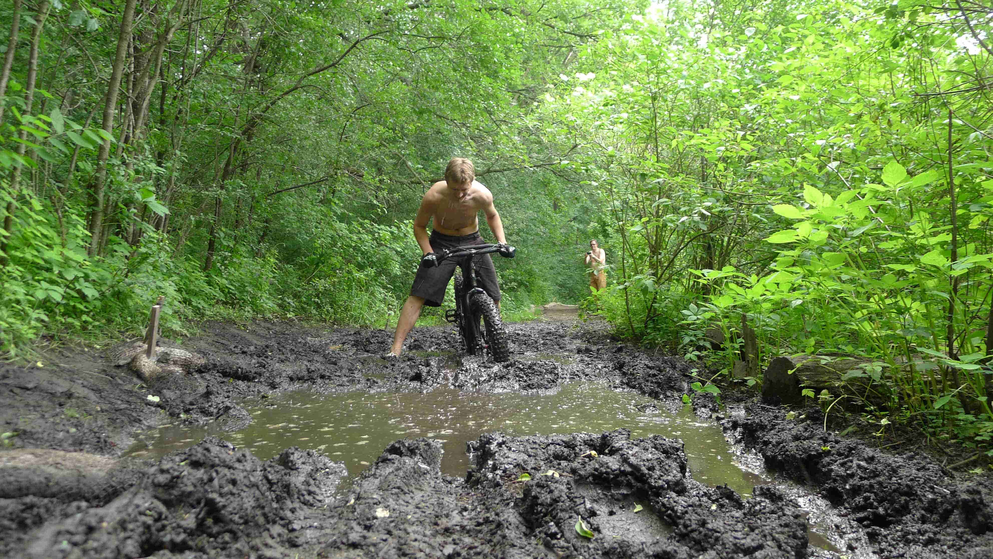 Front view of cyclist on black Surly Moonlander bike, stuck in deep mud on a road in the woods