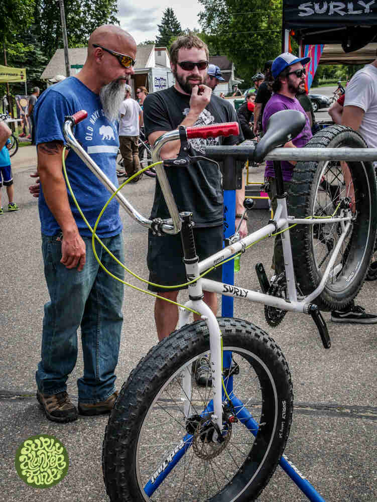 A Surly Pugsley fat bike, white, on a stand, with 2 people looking at it from behind