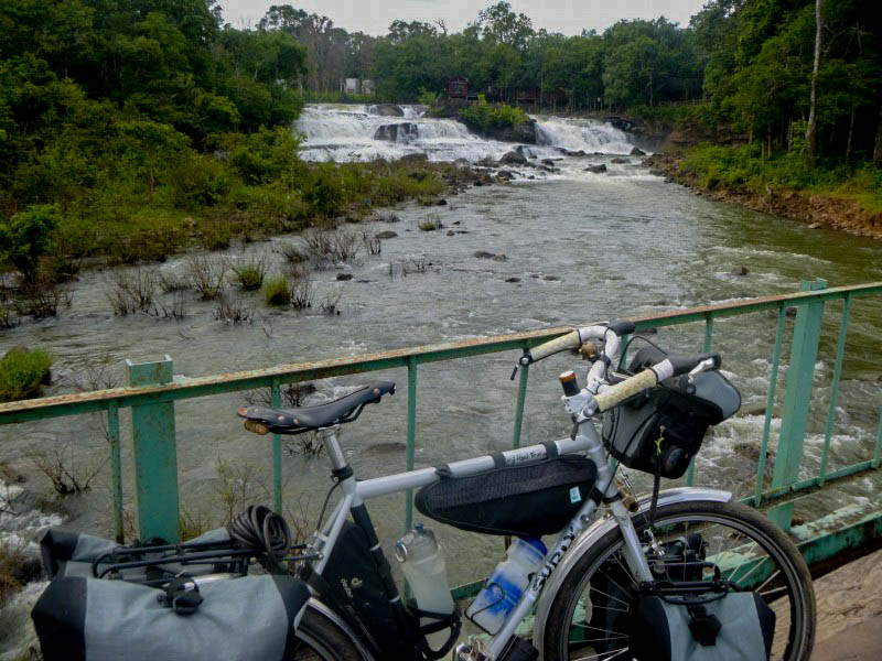 Right side view of a Surly bike with gear, along the rail of a bridge, over a river, with falls in the background