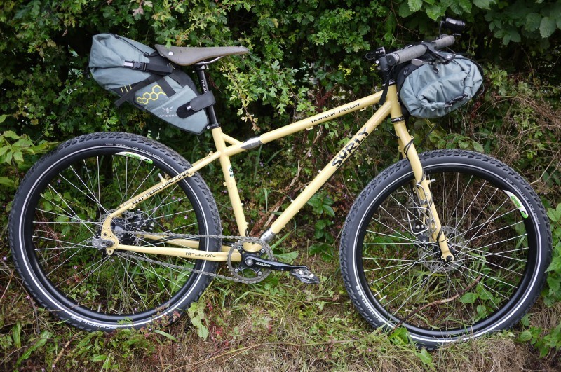 Right profile of a Surly Troll bike with gear packs, parked on grass, in front of hedges