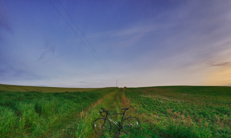 Left side view of a Surly bike, parked on a grassy farm field, with the sun to the right on the horizon
