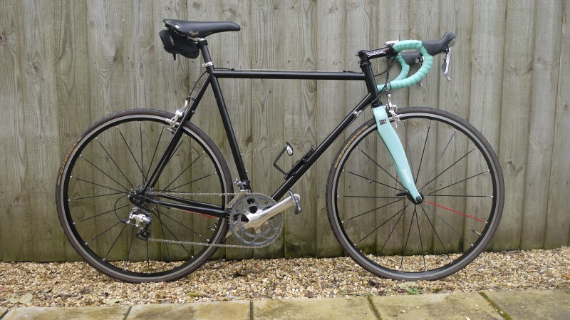 Right side view of a black Surly bike with mint forks, leaning against a wood fence wall