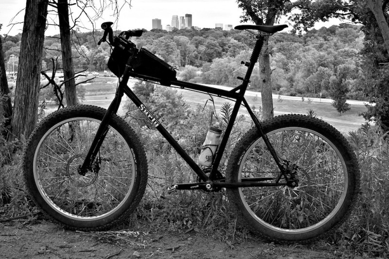 Left view of a Surly bike on a hilltop, overlooking a forest with a city skyline behind it - black and white image