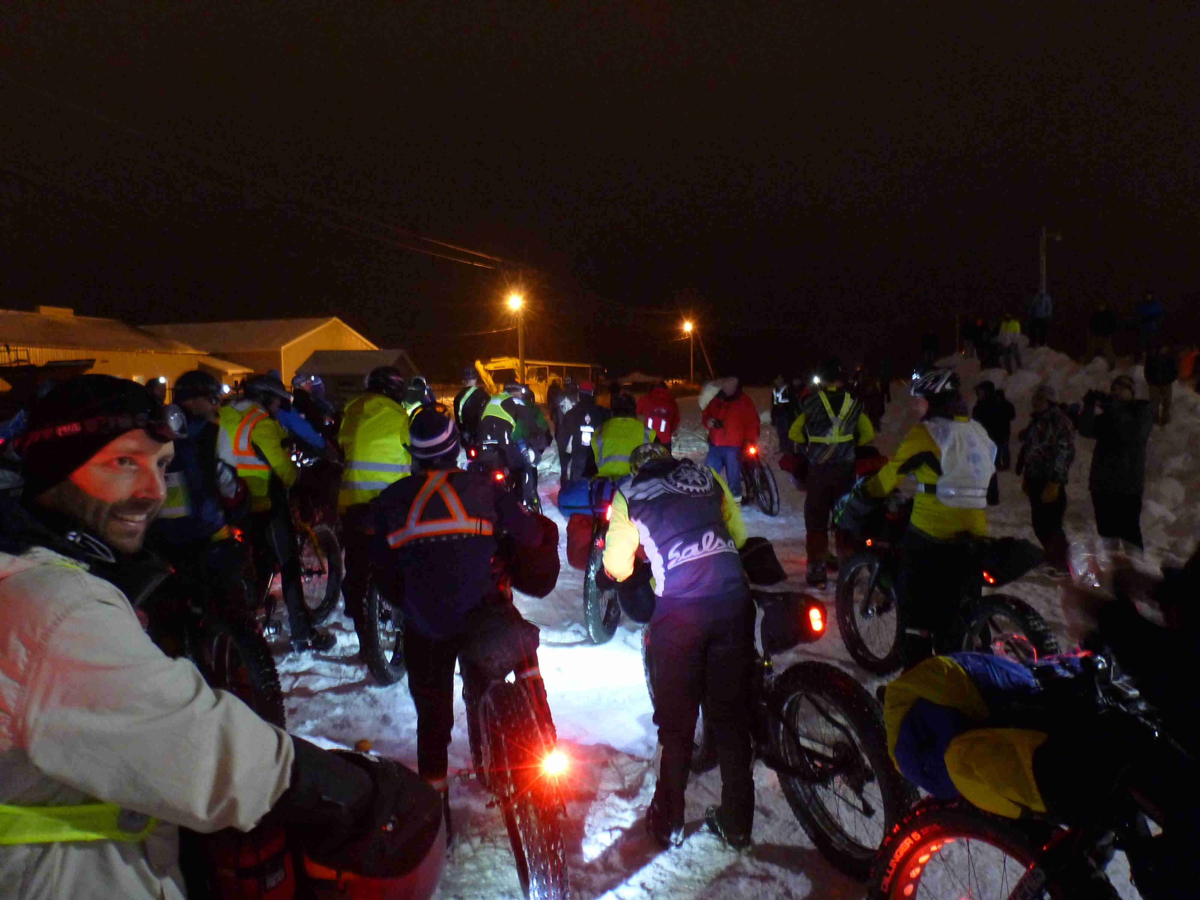 A group of cyclists and their bikes, gathered together on a snow covered lot at night