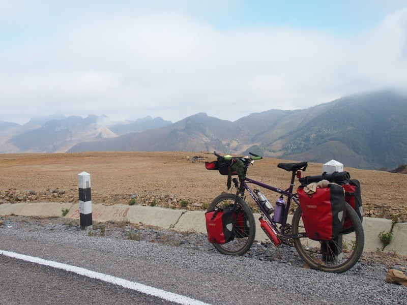 Left side view of a purple Surly bike loaded with gear, on a roadside next to a rock field, with mountains in background
