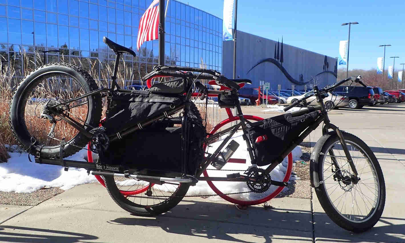 Right side view of a Surly Big Dummy bike hauling a fat bike, parked on a sidewalk in front of an office building