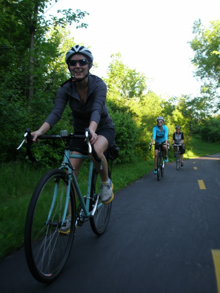 Front, right side view of a cyclist, riding a mint Surly bike, on a paved bike trail in the woods