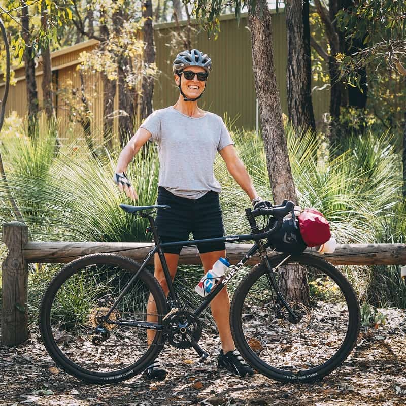 Right profile view of a black Surly Straggler bike in front of a cyclist, with tall grass and trees in background