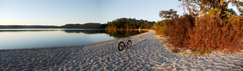 A bike parked along a sand beach, with a lake and trees in the background