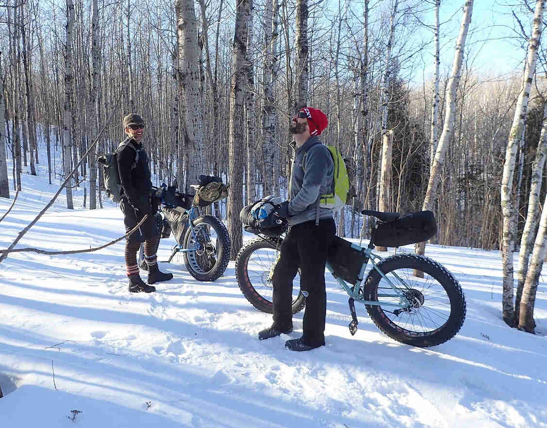 Two cyclists standing in the woods on snow with, their Surly fat bikes