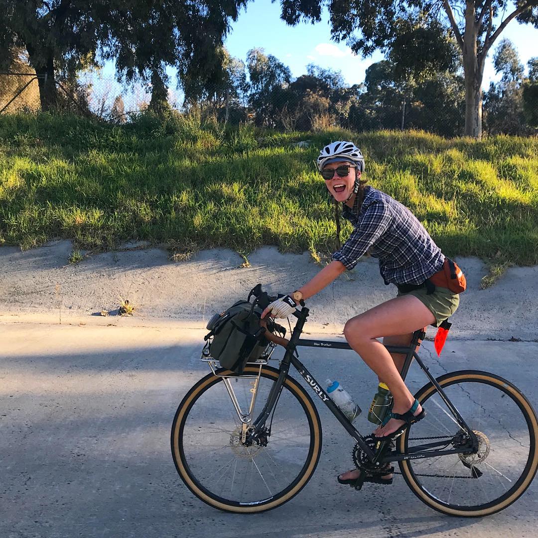 Cyclist smiling at the camera riding a Surly road bike down a paved street with trees in the background