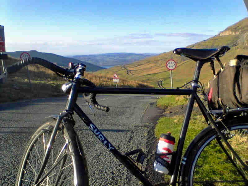 Left side view of a Surly bike, black, parked on the side of a gravel road, in grassy, rolling hills