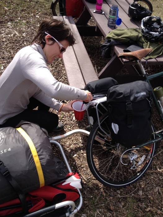 Downward view of a cyclist, wearing a gray Surly Wool Long Sleeve Jersey, dispensing wine from a rear pack on a bike