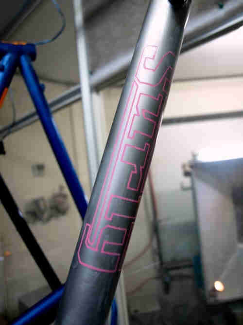 Close up view of a gray bike frame tube, with a pink Surly Bikes logo outline on it
