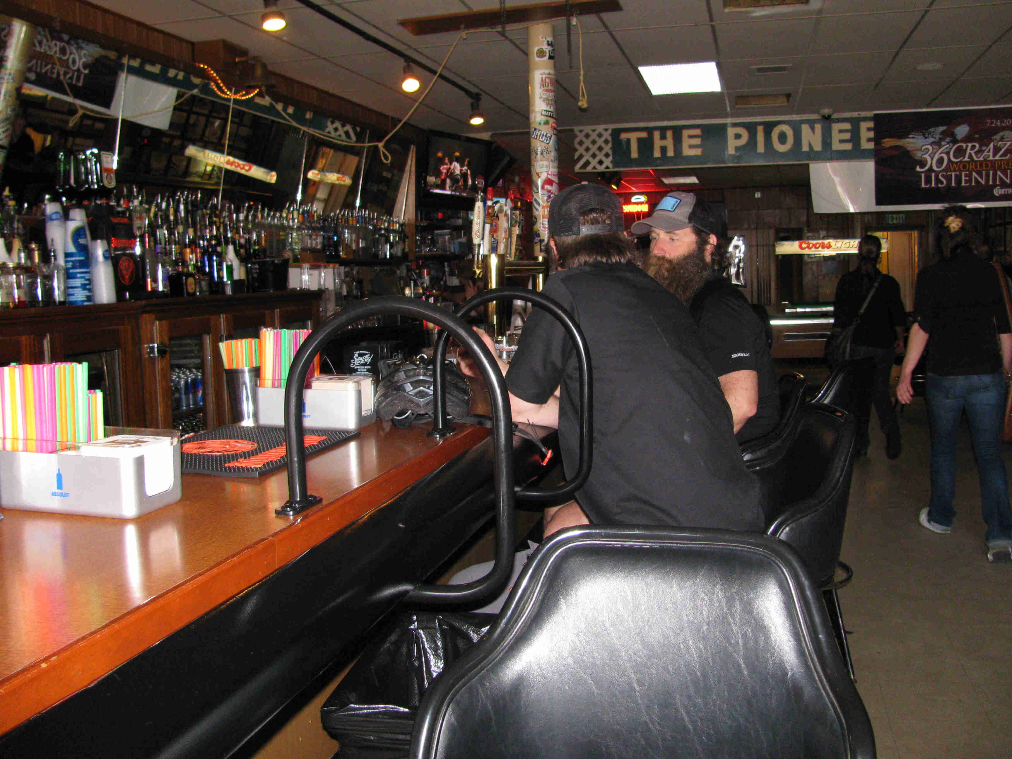 Side view of 2 people, sitting belly up to the countertop and talking, inside a bar