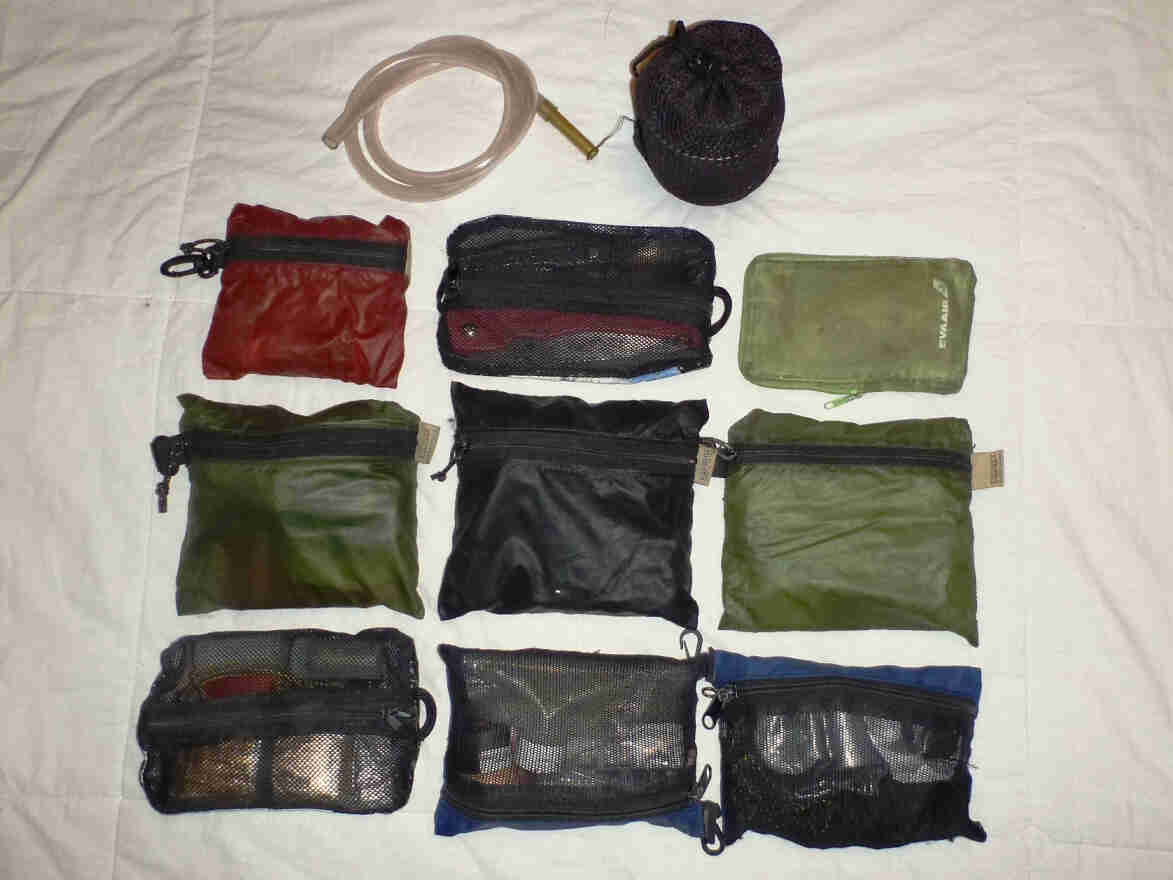 Downward view of 9 zipped up pouches and a couple other items, laying on a flat white surface