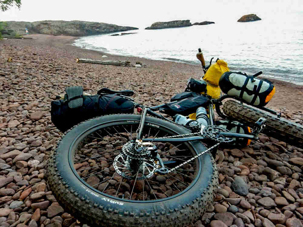 Ground level view of a black Surly Pugsley fat bike, laying on a rocky seashore