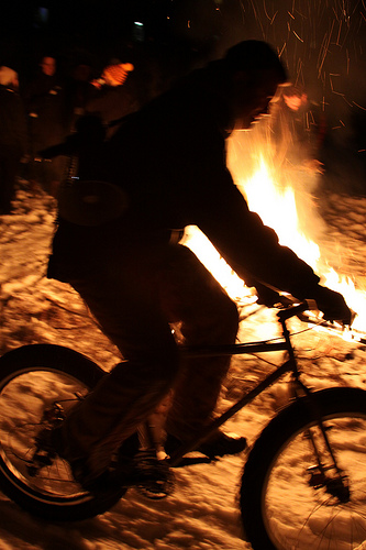 Right side view of a cyclist riding a Surly Pugsley fat bike on snow, around a campfire at night