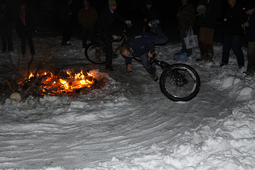 Front view of a cyclist, riding a Surly Pugsley fat bike and falling to the snow, next to a campfire at night