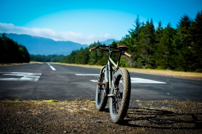 Rear view of a Surly Pugsley fat bike, facing down a paved runway, with trees and mountains in the background