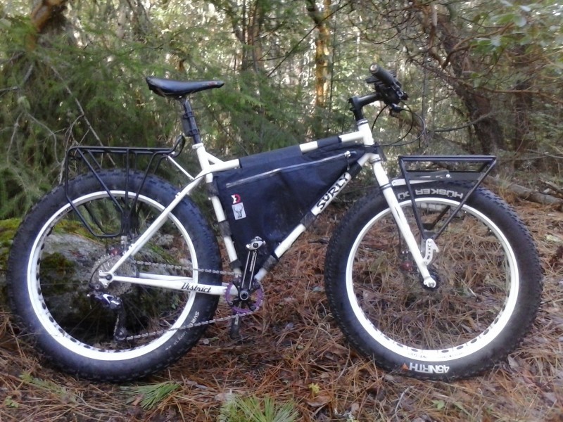 Right side view of a white Surly Pugsley fat bike with frame bag, parked on pine needles in the forest