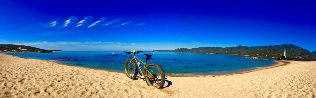Panoramic rear view of a Surly Pugsley fat bike, parked on a beach, in front of a blue water bay