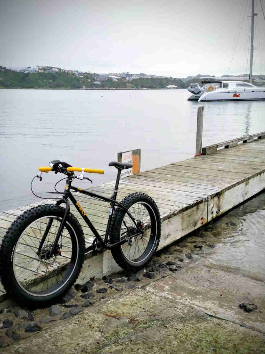 Left side view of a black Surly Pugsley fat bike, parked next to dock on a bay