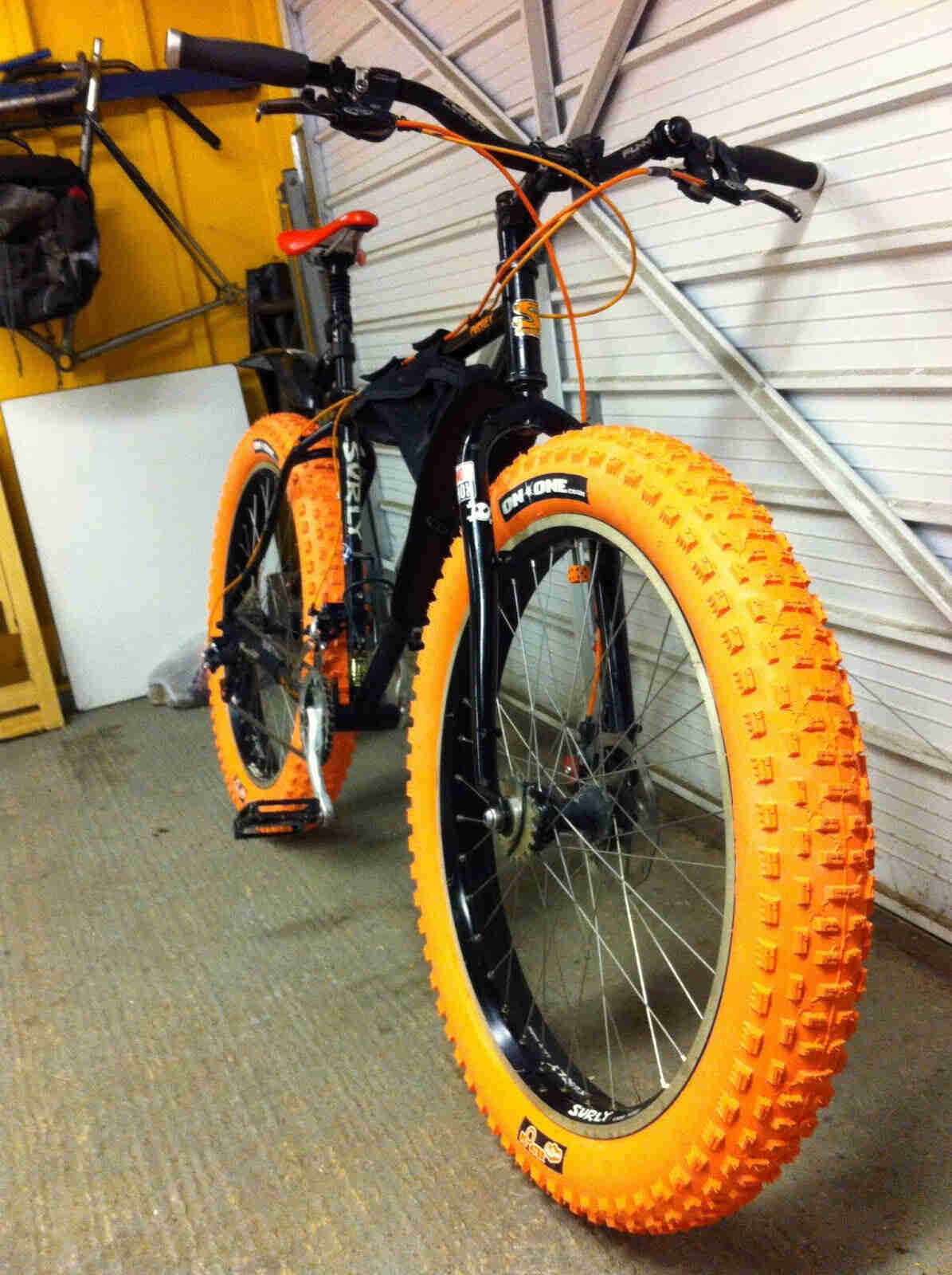 Front view of a black Surly Pugsley fat bike with orange tires and offset forks, against a garage door - on the inside
