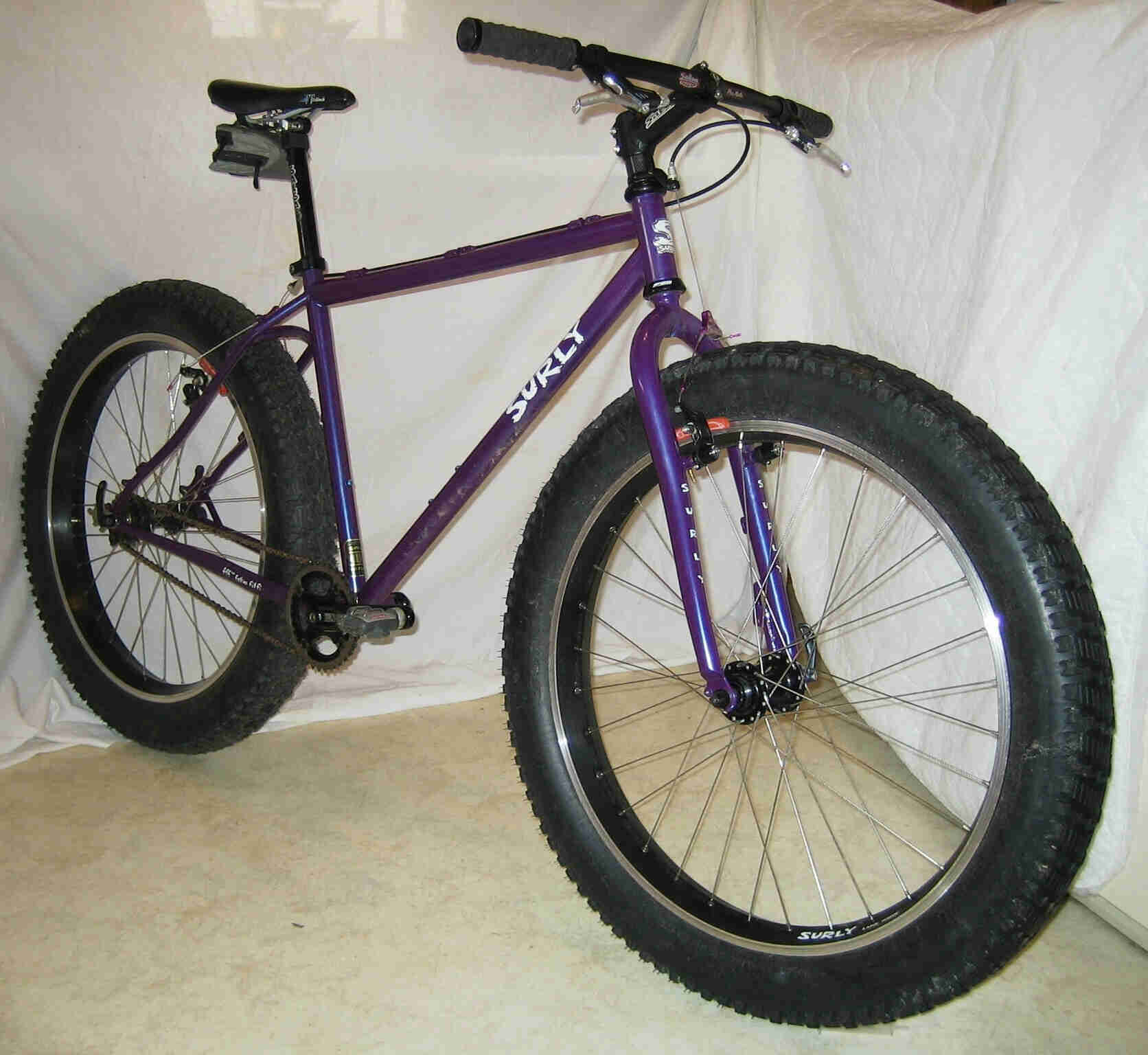 Front, right side view of a purple Surly Pugsley fat bike. on cement floor, with white sheet wall behind it