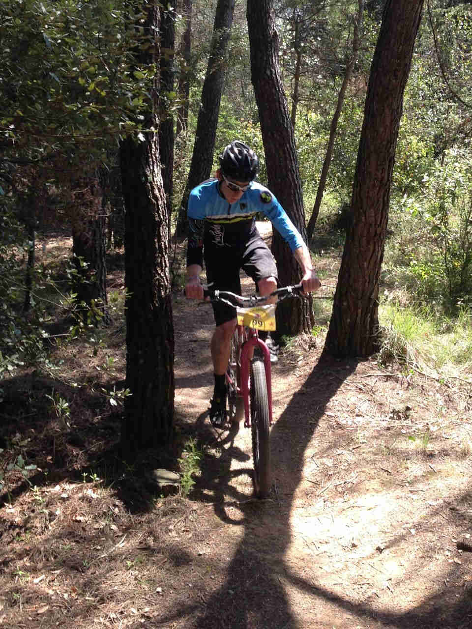 Front view of a cyclist, riding a pink Surly bike up a hill, on a dirt trail in the woods