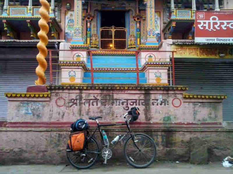 Right profile of a Surly bike, loaded with gear, on a sidewalk in front of a colorful asian style building