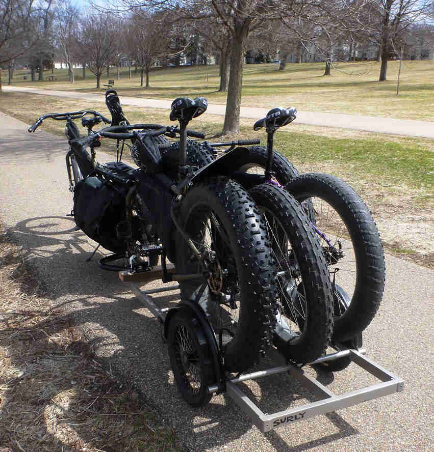 Rear, left side view of 2 Surly fat bikes, loaded on trailer behind a Surly Big Dummy bike, on a paved trail